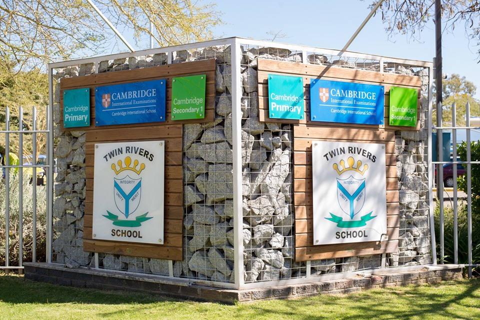 The Twin Rivers School entrance sign with the school crest and Cambridge International accreditation panels